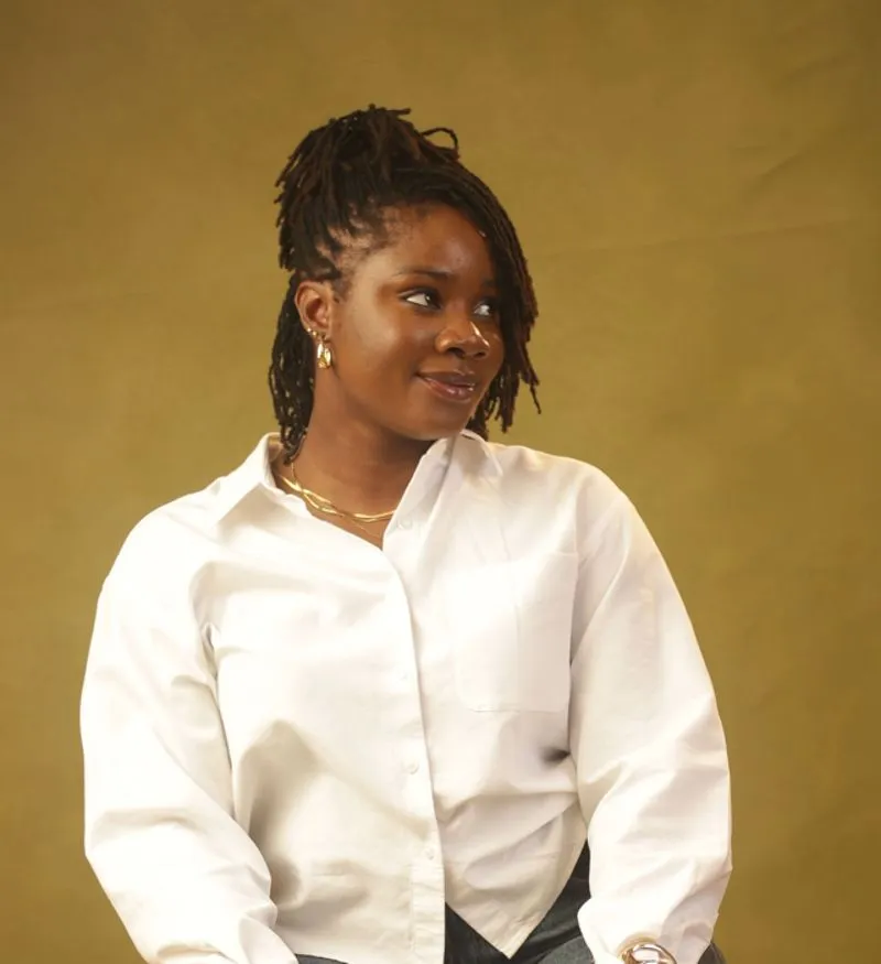 Olubukola seated on a wooden stool in a white shirt and jeans